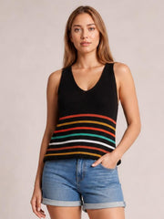 Model wears a black striped V-neck knit tank with multicolor horizontal bands, sleeveless construction, and a relaxed silhouette, posing with one hand in her shorts pocket.
