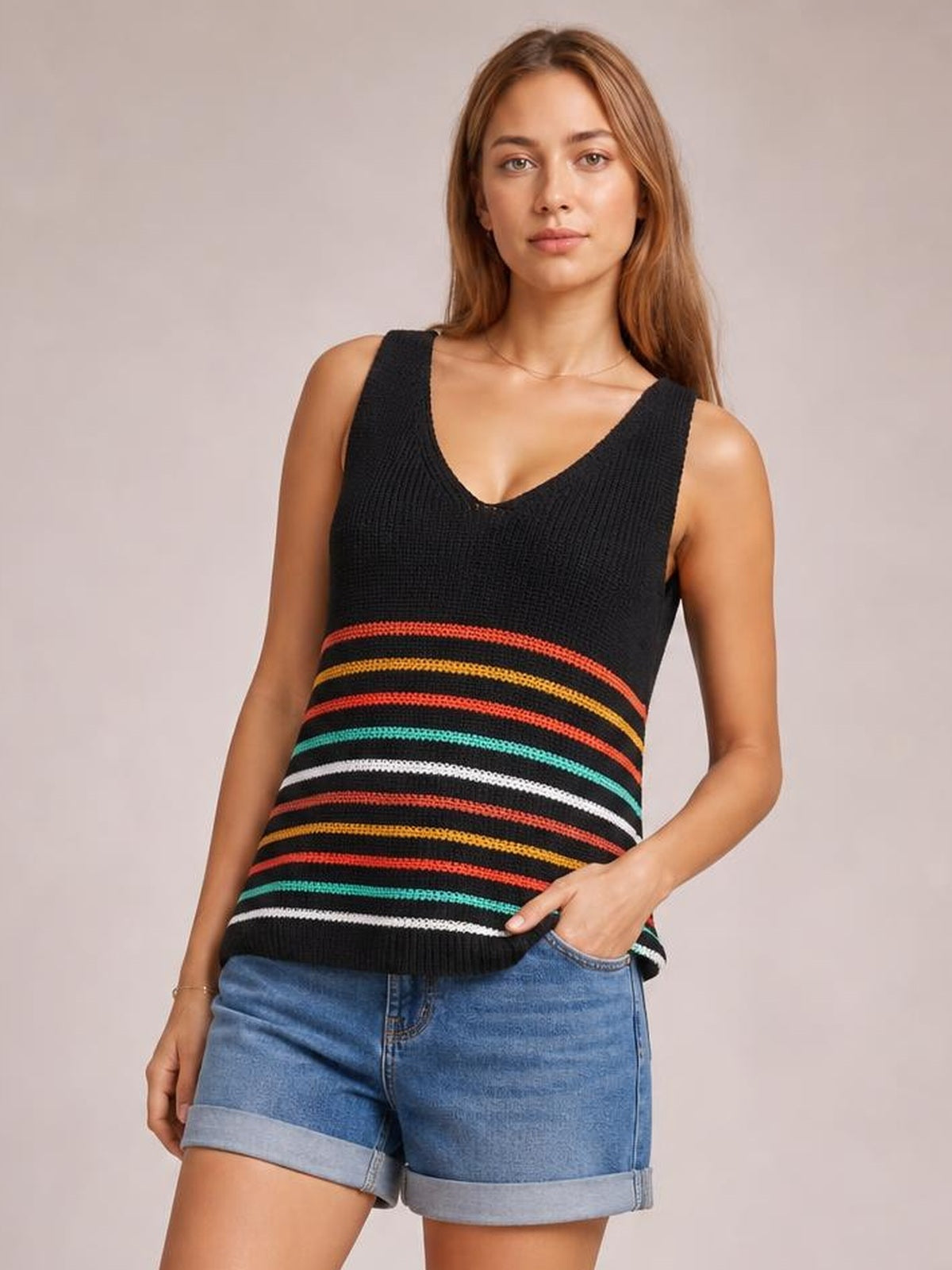 Model wears a black striped V-neck knit tank with wide shoulder straps, multicolor horizontal bands, a relaxed silhouette, and one hand in her shorts pocket.