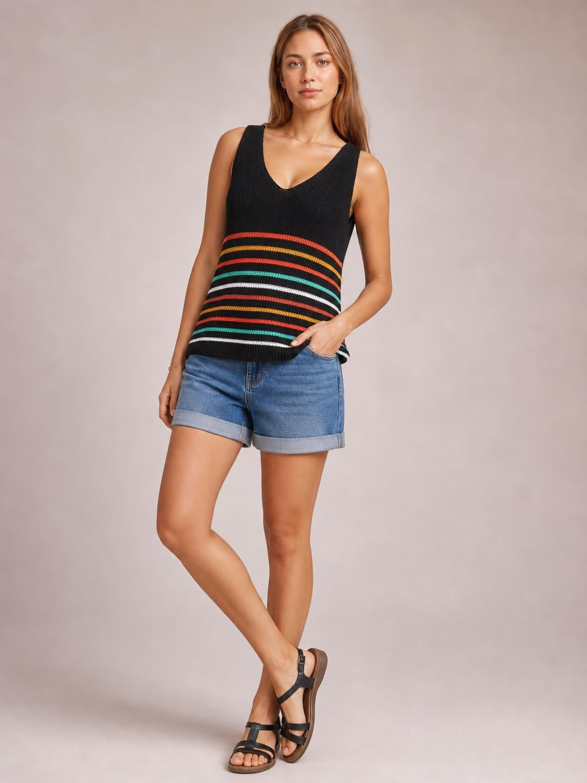 Model wearing a black striped V-neck knit tank with colorful horizontal bands, wide shoulder straps, and a relaxed straight silhouette, posing with one hand in her shorts pocket.
