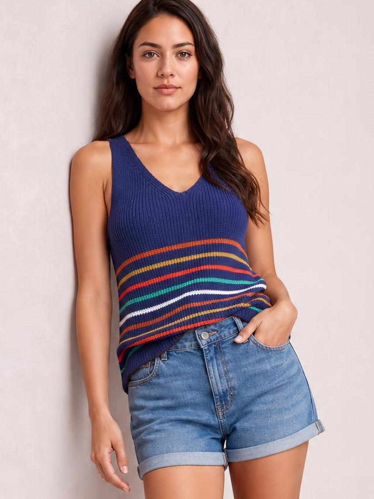 Model wearing a navy striped V-neck knit tank with colorful horizontal bands, wide shoulder straps, and a relaxed silhouette, posing with one hand in her pocket.