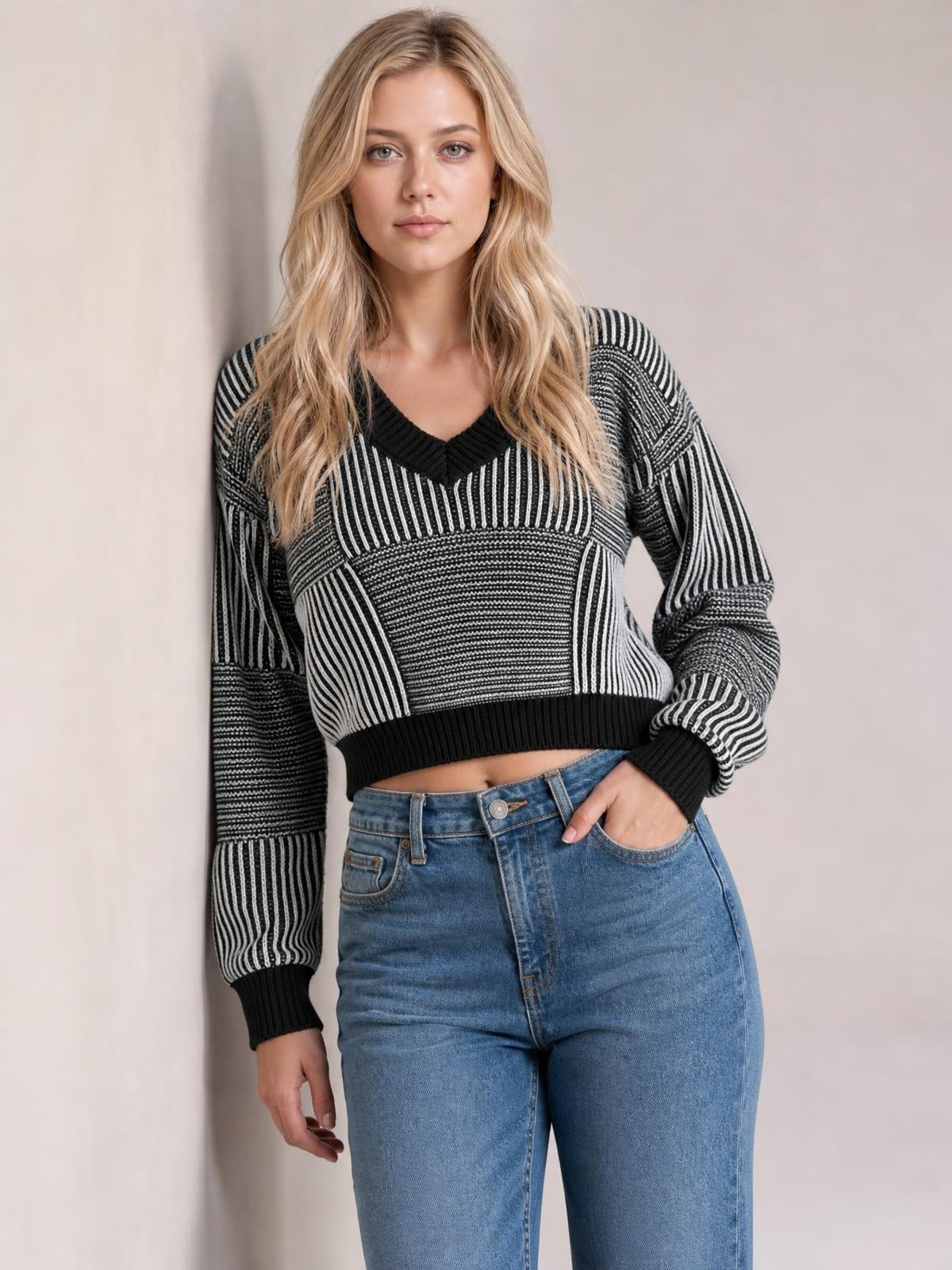 Model wearing a black and white striped V-neck long sleeve sweater with a cropped silhouette, ribbed cuffs and hem, posing with one hand in her jeans pocket.