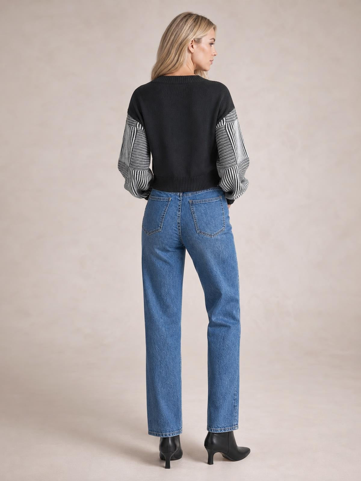 Model shown from behind wearing a black long-sleeve sweater with contrasting striped sleeves, ribbed neckline and hem, and a relaxed silhouette.