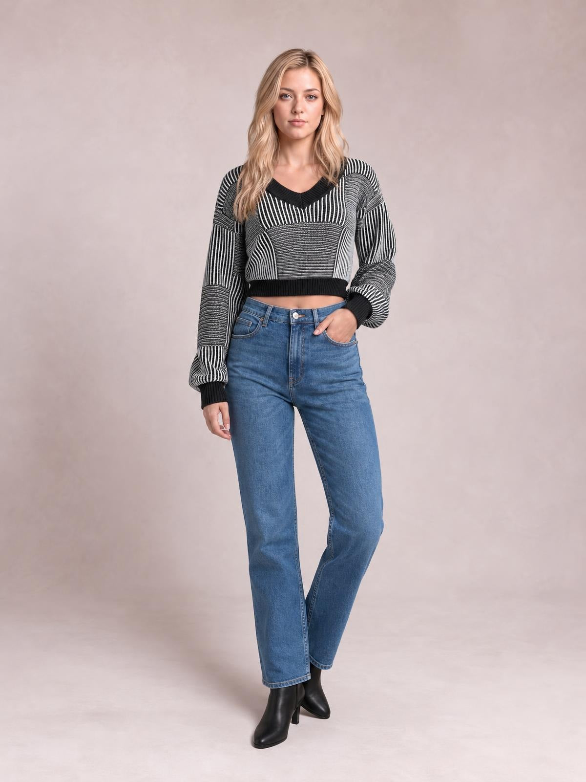 Model poses in a black-and-white striped V-neck long sleeve sweater with ribbed cuffs and hem, a cropped silhouette, and bold geometric knit panels.