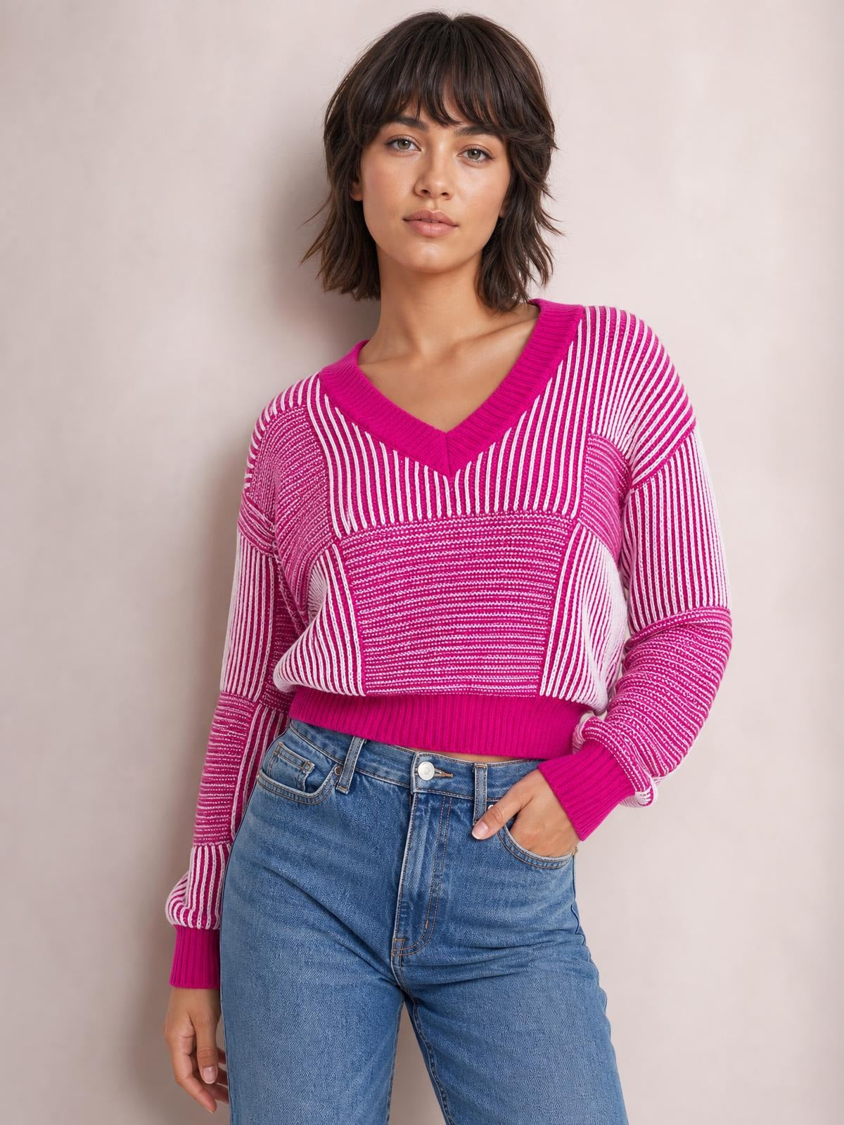 Model wearing a pink and white striped V-neck long sleeve sweater with ribbed trim, relaxed silhouette, and one hand tucked into her jeans pocket.