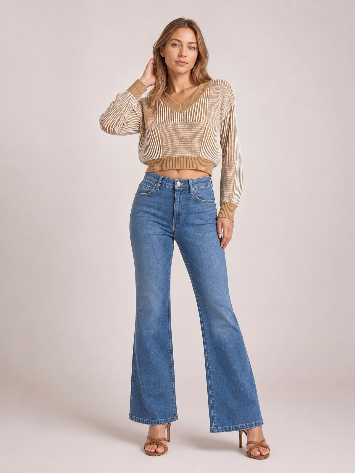 Model poses in a tan striped V-neck long sleeve sweater with ribbed cuffs and hem, a cropped relaxed silhouette, and contrasting vertical and horizontal knit patterns.