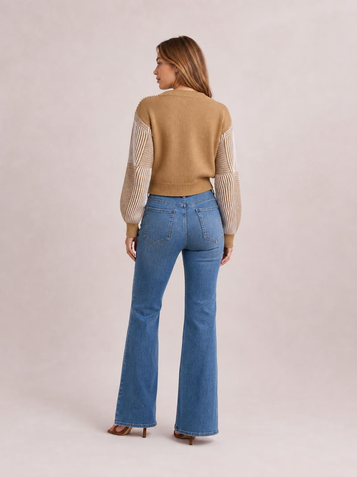 Model shown from the back wears a camel striped long sleeve sweater with contrasting striped sleeves, ribbed cuffs and hem, and a cropped silhouette.