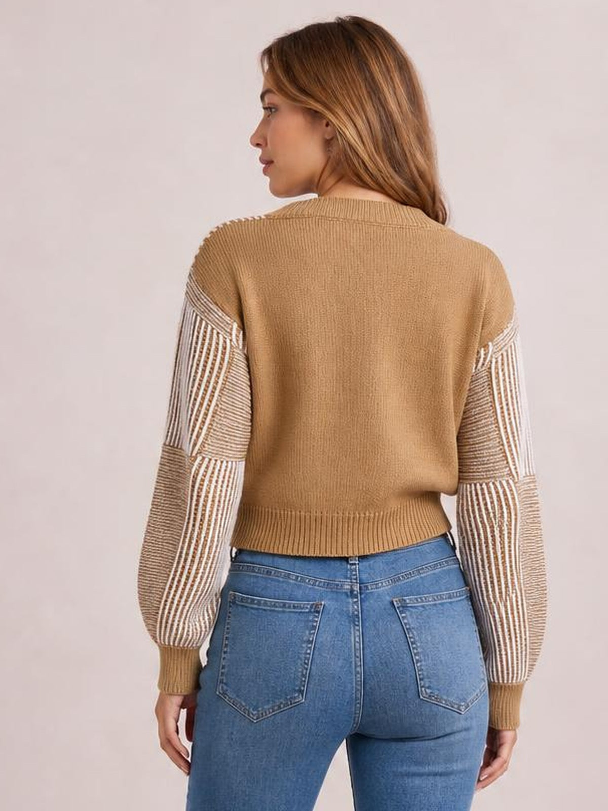 Model shown from the back wearing a camel striped V-neck long sleeve sweater with contrasting ribbed sleeves, a relaxed silhouette, and ribbed cuffs and hem.