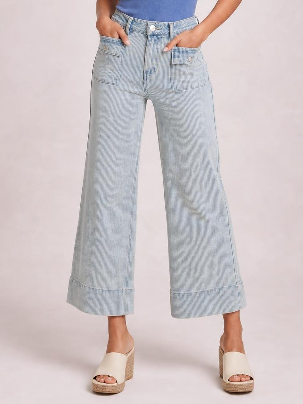 A model poses with hands in the pockets of light blue striped wide-leg cropped jeans featuring a structured waistband, button closure, patch pockets, and cuffed hems.