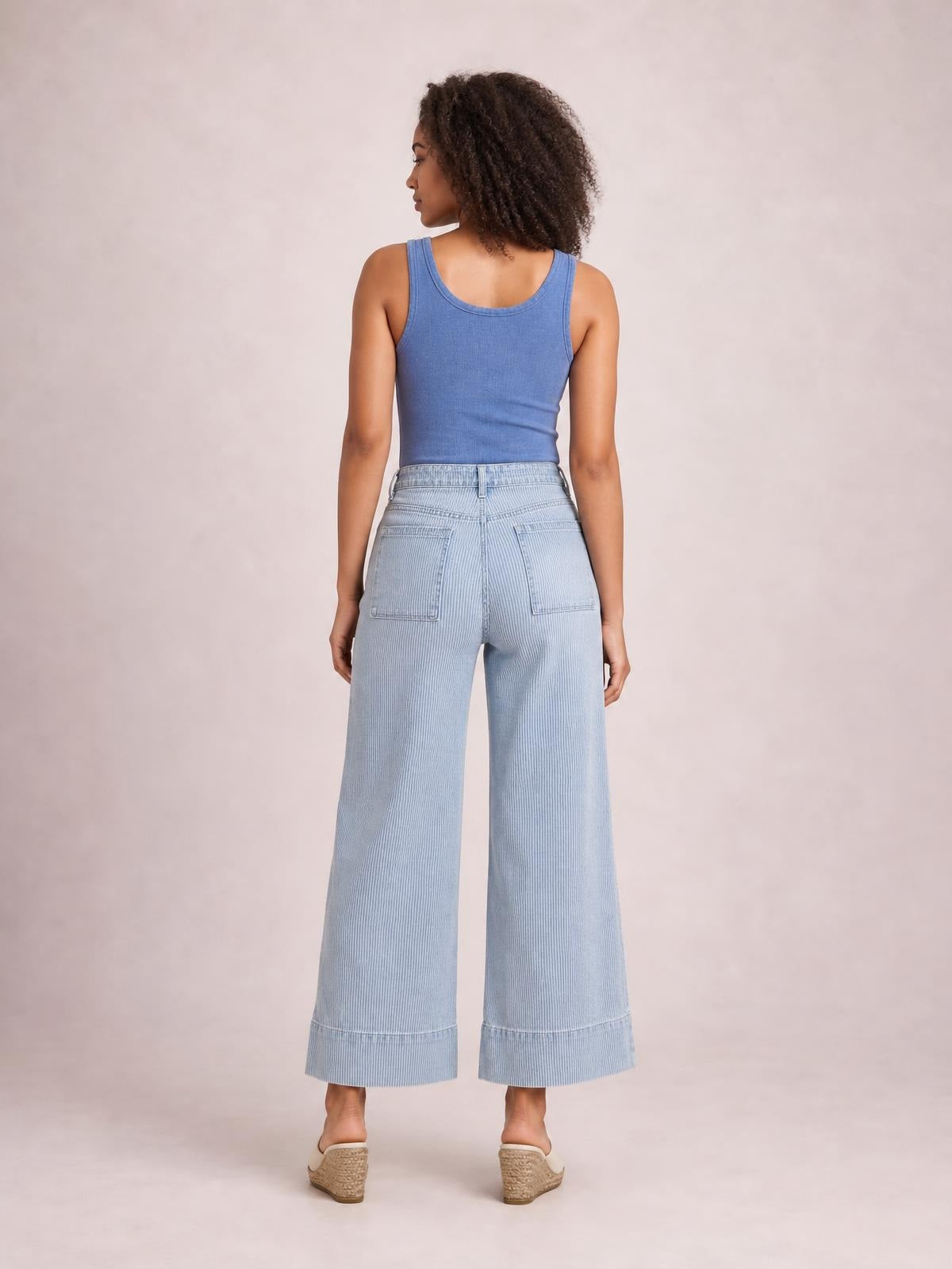 A model stands facing away in light blue striped wide-leg cropped jeans with a high waistband, belt loops, and two back patch pockets.