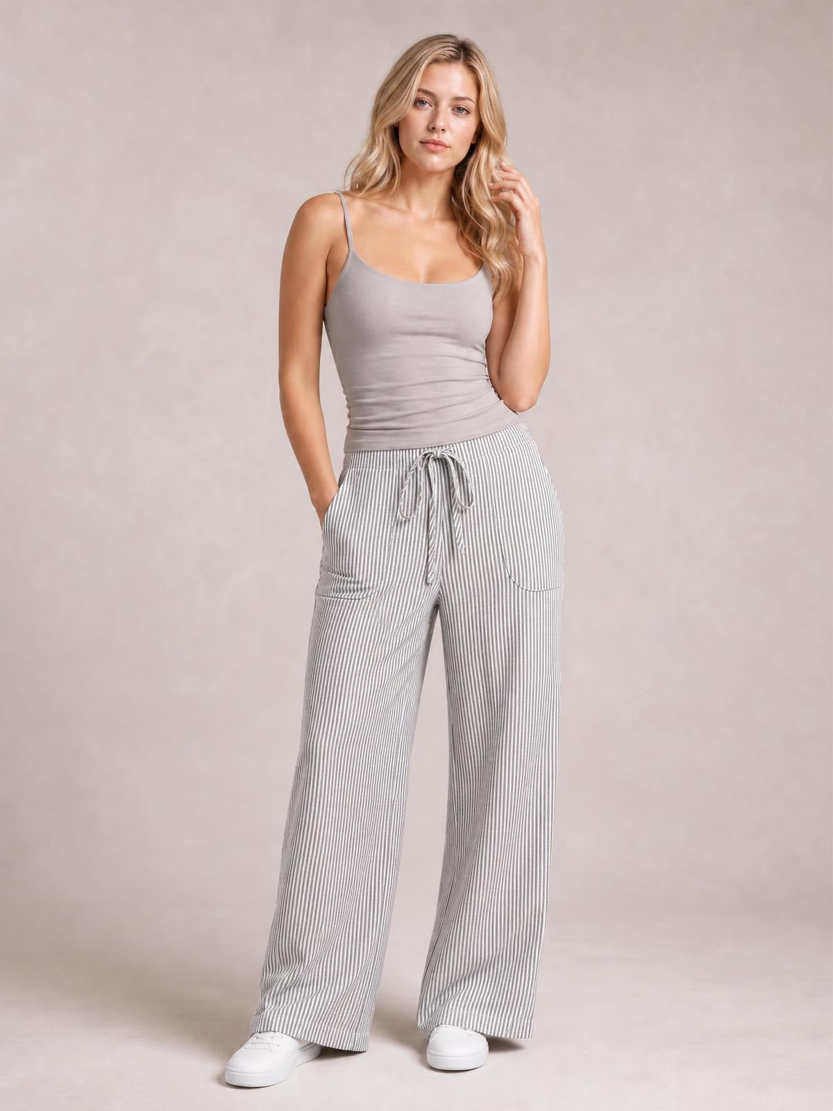 Model poses in gray-and-white striped wide-leg pants with a drawstring waist and curved front pockets, styled with a fitted camisole.
