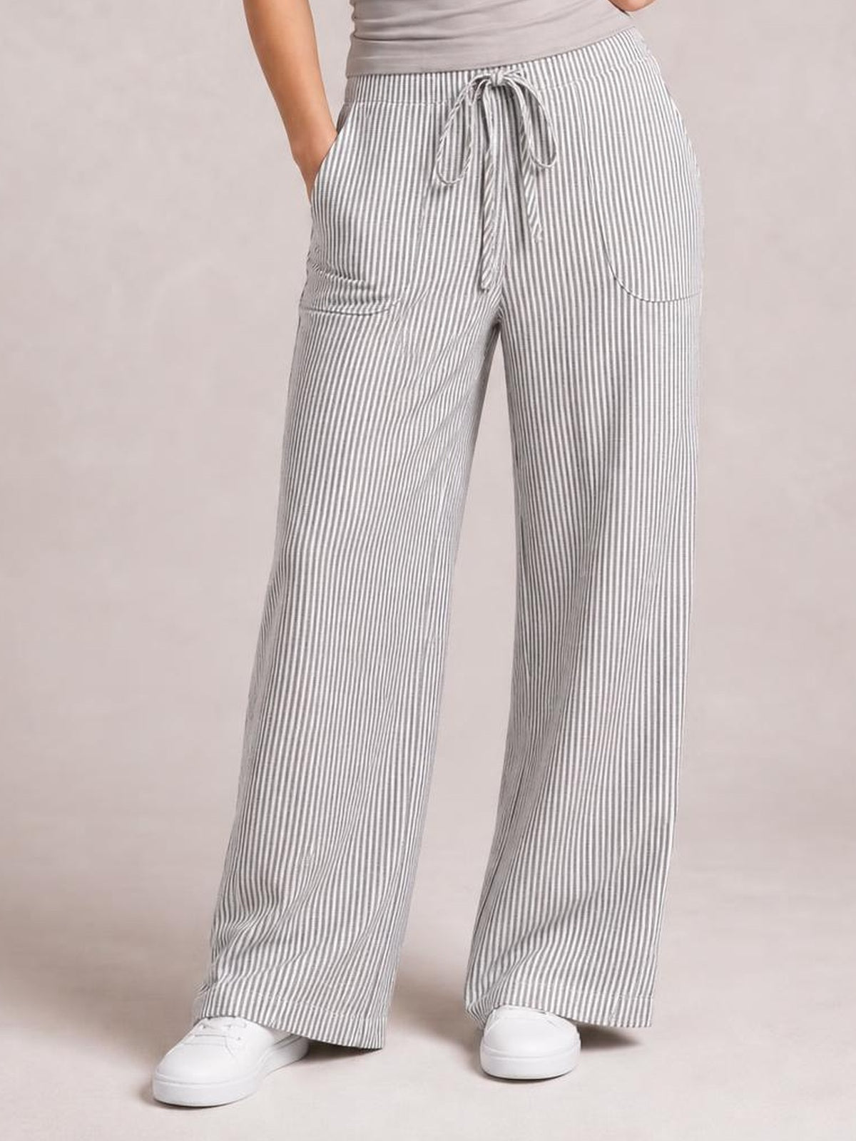 Model wearing gray-and-white striped wide-leg pants with a drawstring waist, curved front pockets, and a relaxed full-length silhouette.