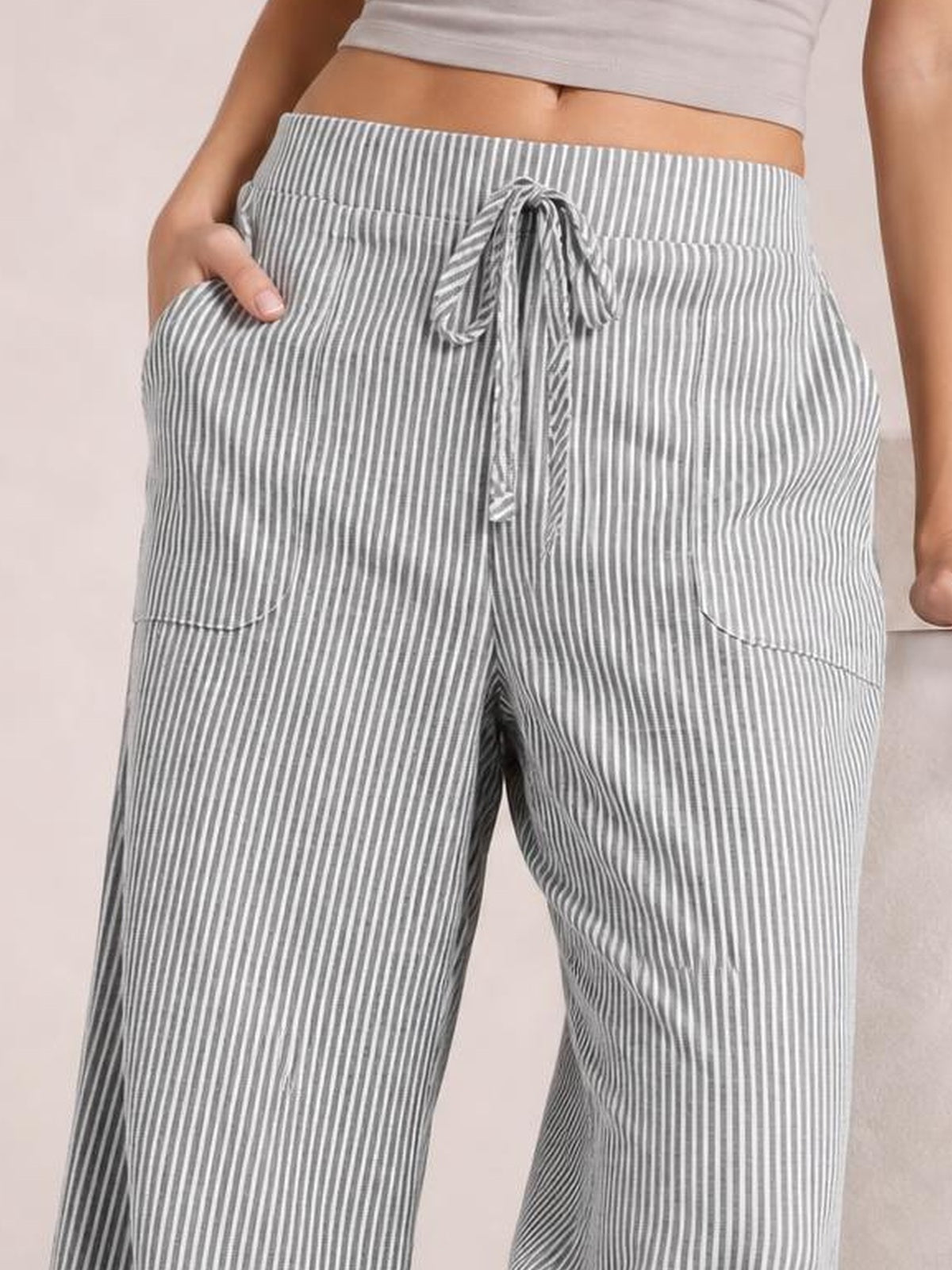 Model wearing gray-and-white striped wide-leg pants with a drawstring waist and large patch pockets, shown with one hand tucked into a pocket.