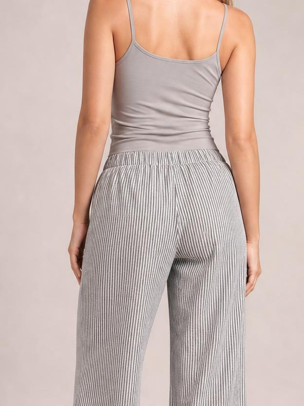 A model stands with hands at her sides, showing gray striped wide-leg pants with a gathered elastic waistband, relaxed silhouette, and side pockets.