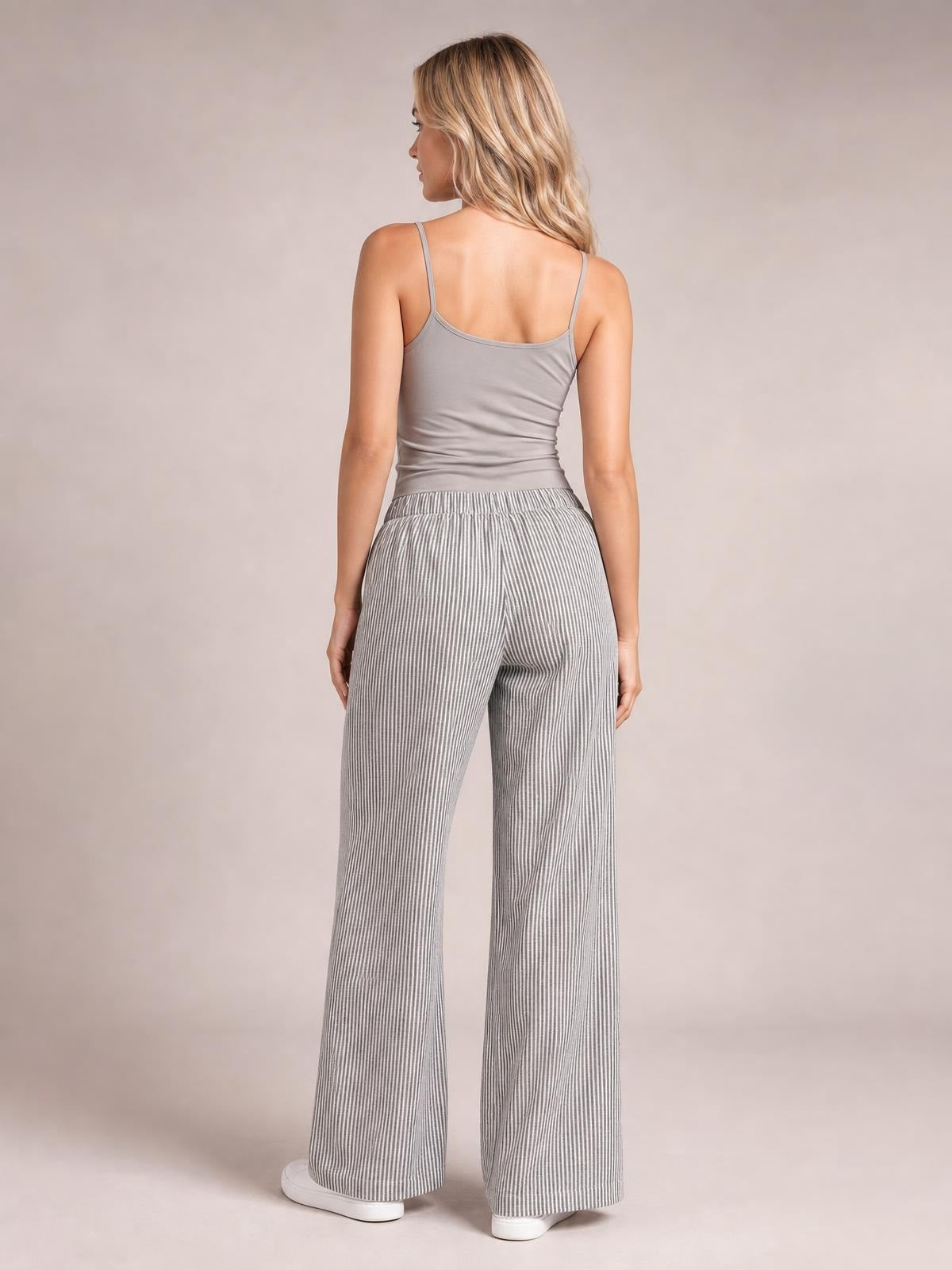 A model stands in a back view wearing gray-and-white striped wide-leg pants with a relaxed silhouette and gathered elastic waistband.
