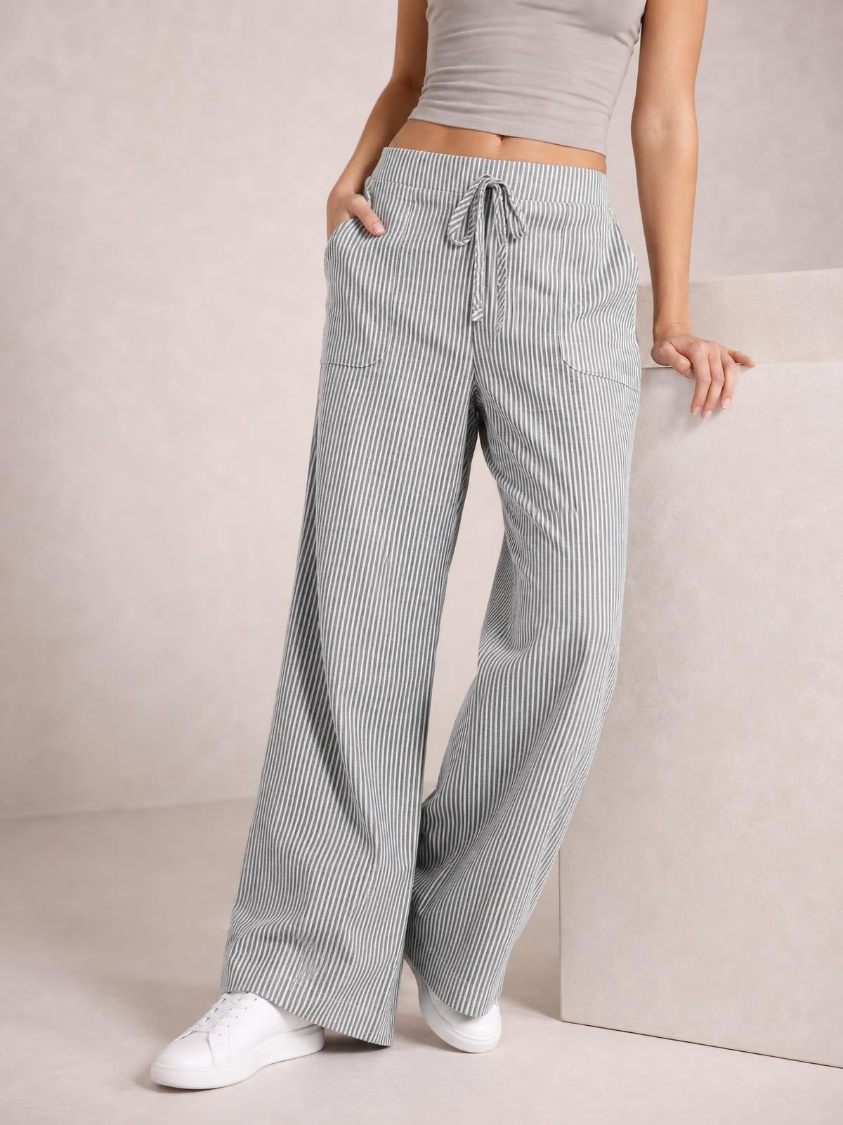 Model wearing gray-and-white striped wide-leg pants with a drawstring waist and side pockets, posing with one hand in a pocket.