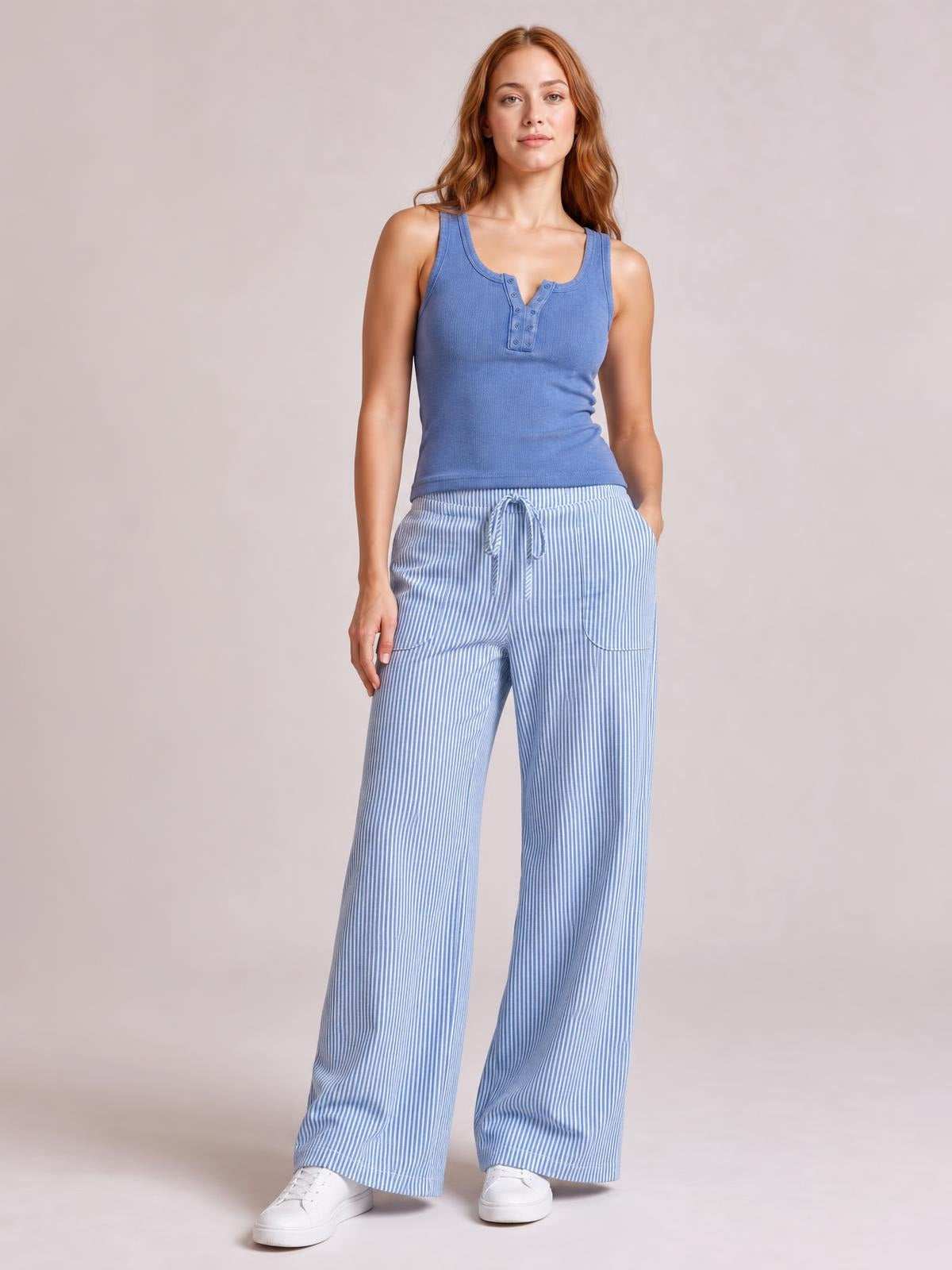 Model standing in light blue striped wide-leg pants with a drawstring waist, curved front pockets, and a relaxed full-length silhouette.