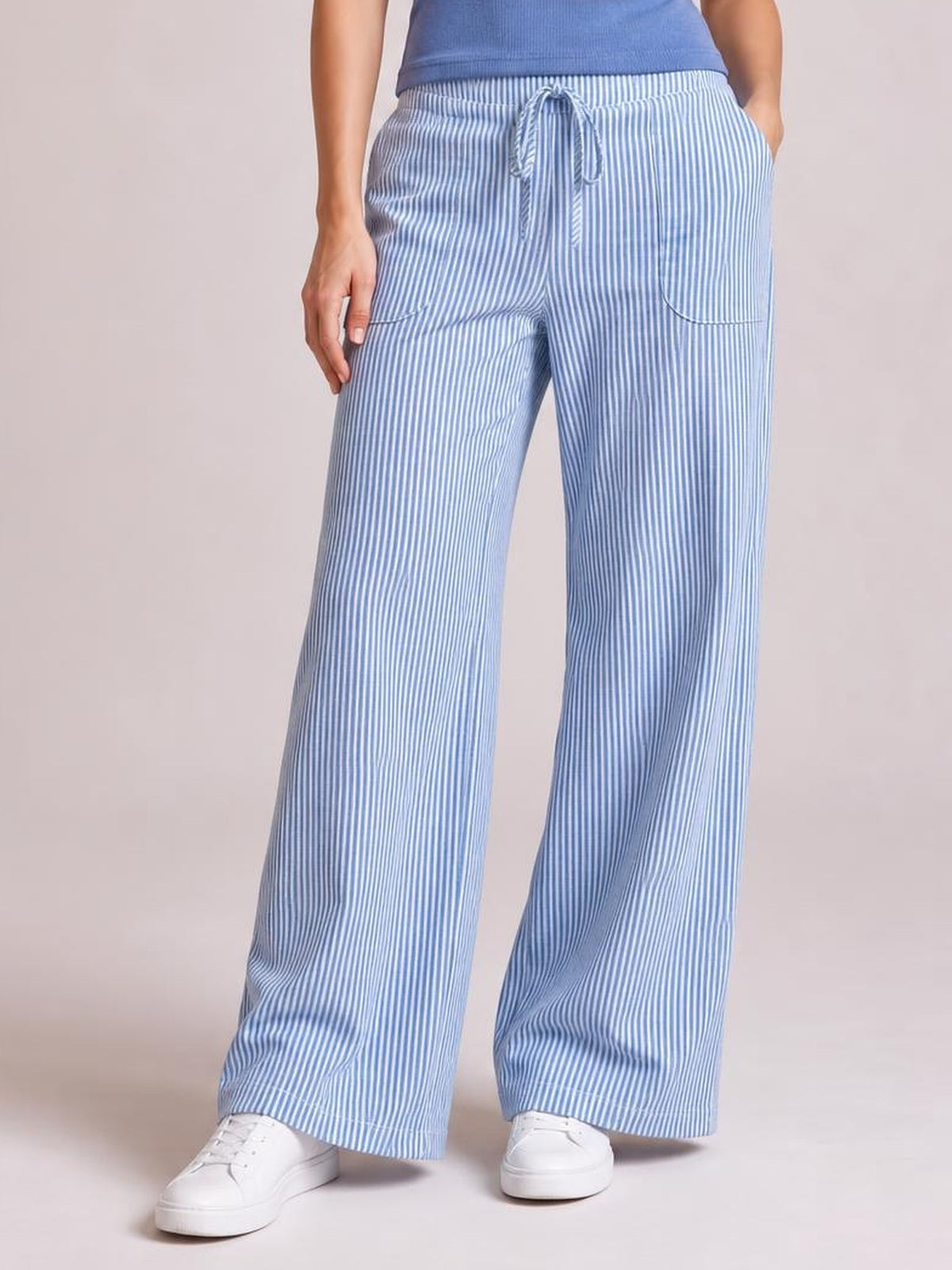 A cropped model wears light blue and white vertically striped wide-leg pants with an elastic drawstring waist, front pockets, and a relaxed silhouette.