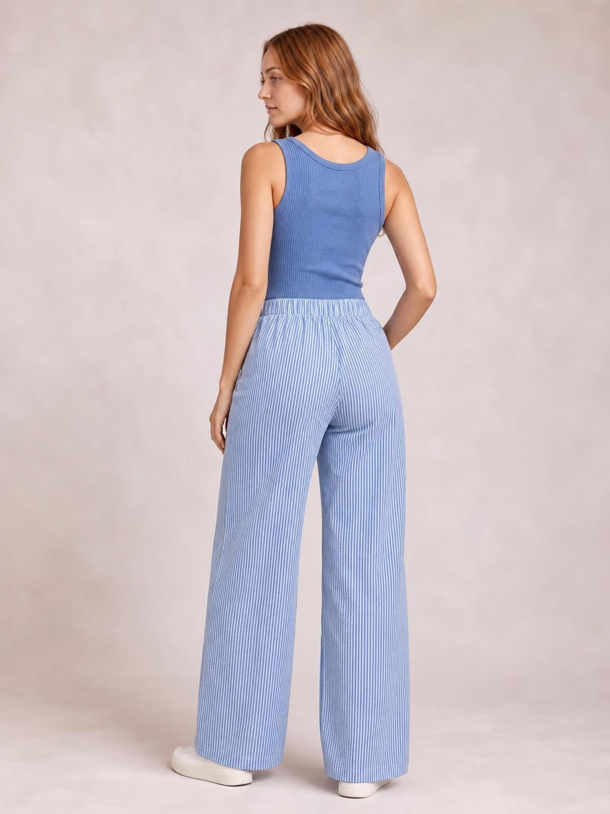 Model turned slightly away wears blue-and-white striped wide-leg pants with an elastic waistband and side pockets, shown in a relaxed standing pose.