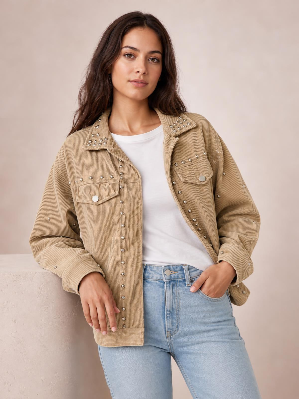 Model poses in a tan corduroy collared button-up jacket with studded detailing, flap pockets, long sleeves, and a relaxed silhouette.