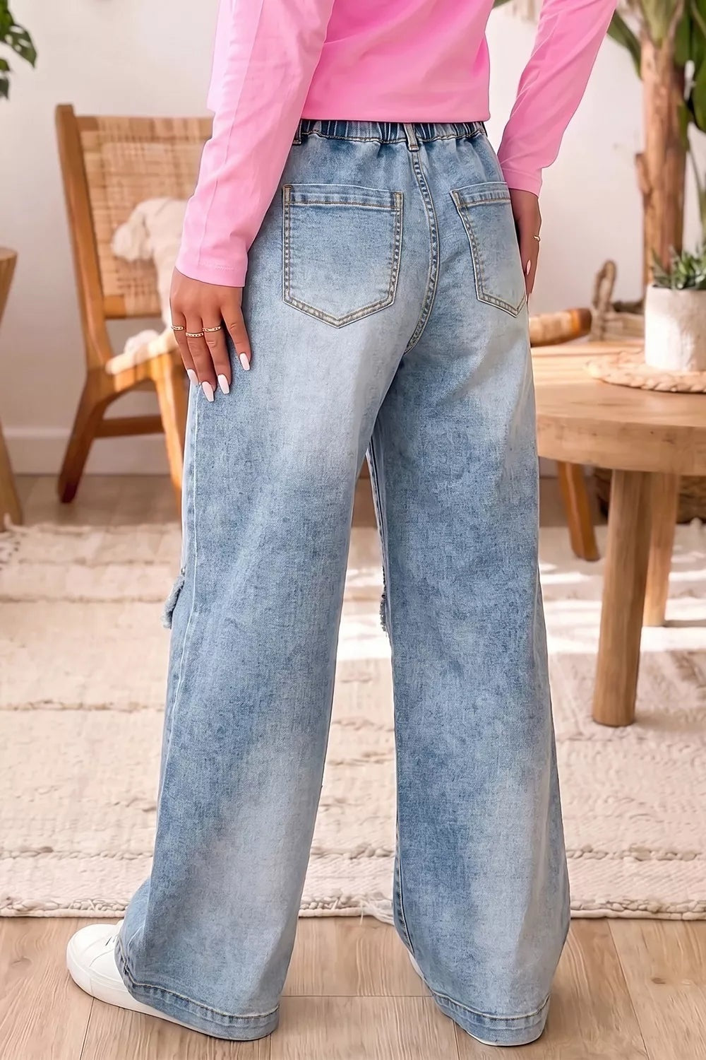 A model poses from behind in light blue washed wide-leg jeans with a gathered waistband, belt loops, and two outlined patch pockets.