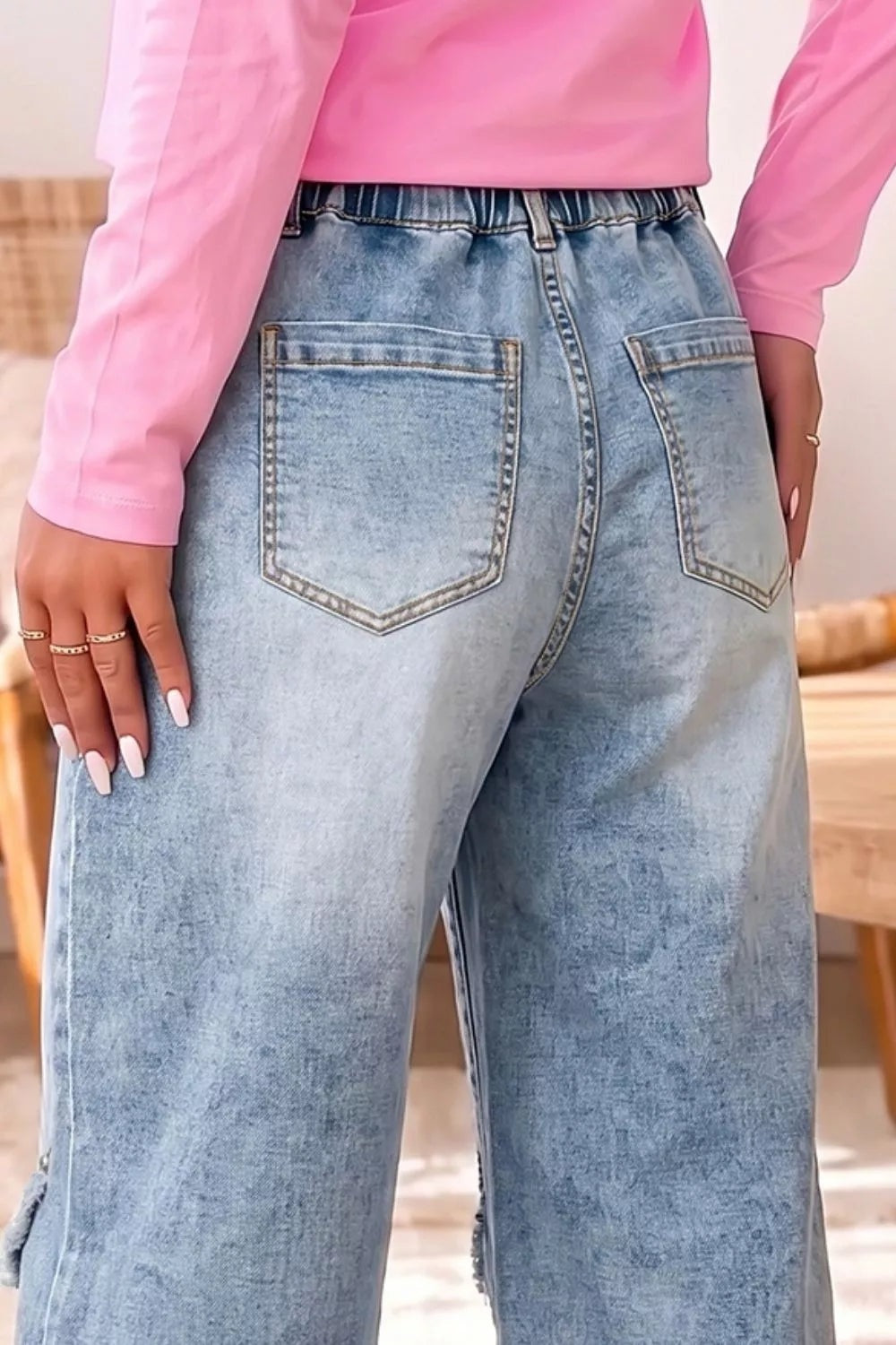 A model wears light blue washed studded-detail wide-leg jeans with large patch pockets, belt loops, and a structured waistband, resting one hand on the hip.