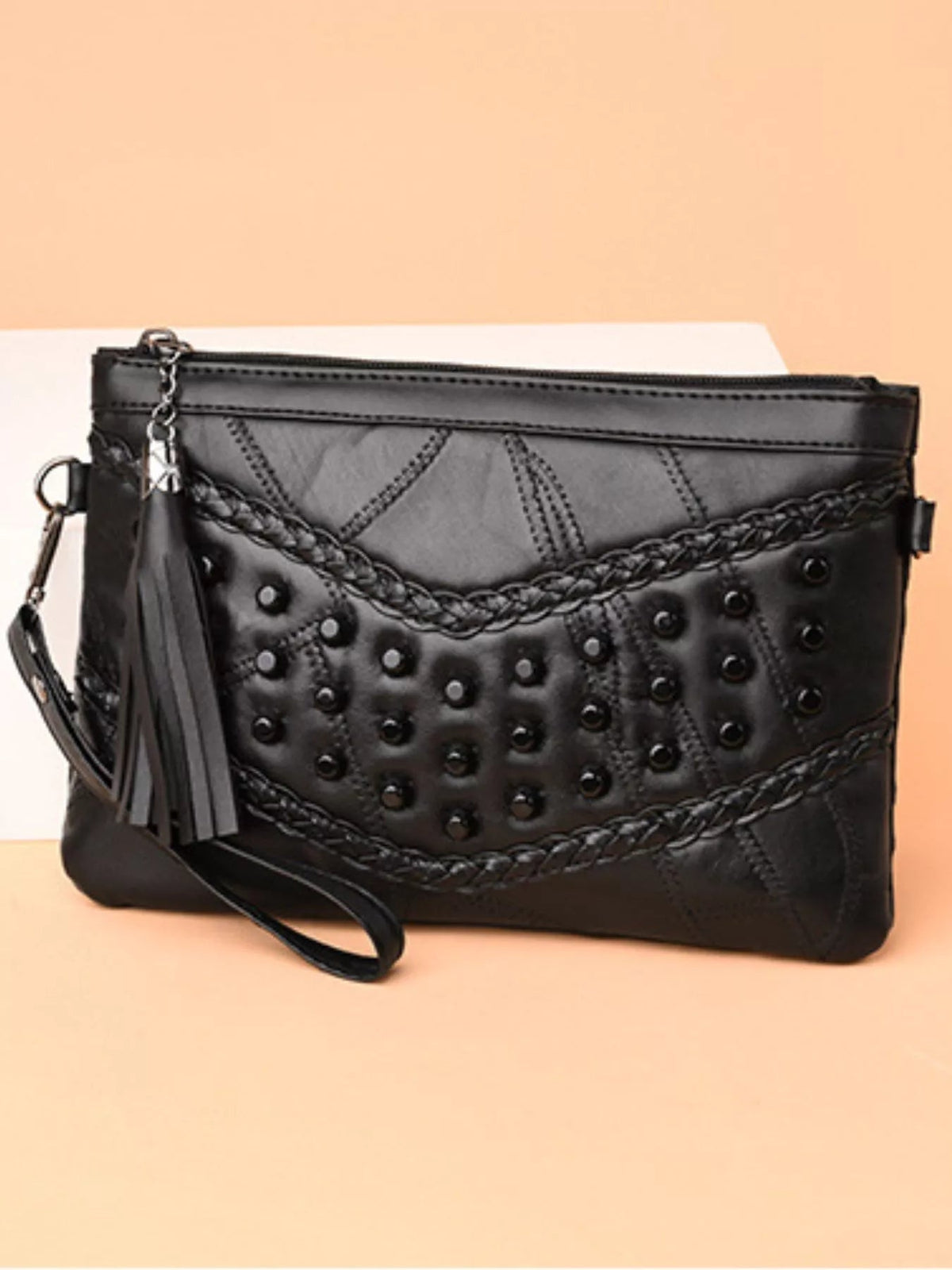 Black medium PU leather crossbody bag with studded front, braided trim, top zipper, and a long tassel detail.
