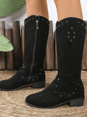 Model wearing black studded mid-calf boots with low block heels, rounded toes, textured panels, and visible side zipper closures.
