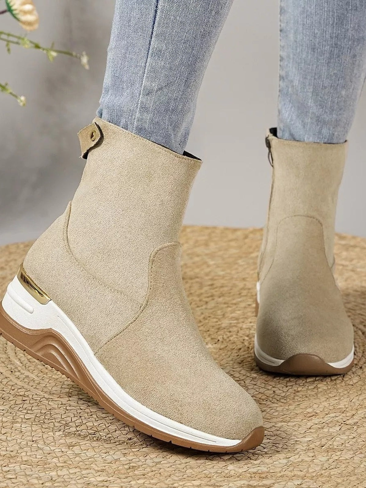 A model wears beige suede ankle boots with mid-height wedge heels, rounded toes, white rubber midsoles, brown outsoles, and visible stitched panel construction.
