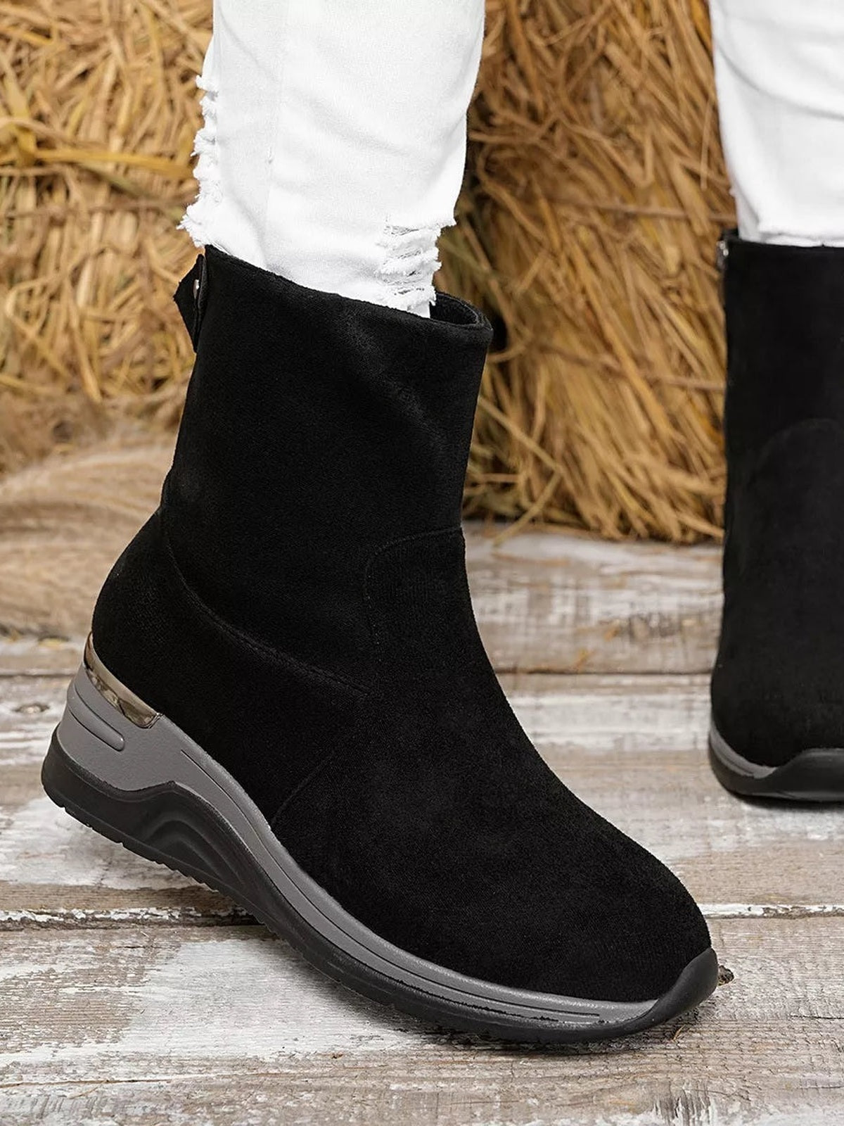 Black suede ankle boots with rounded toes, mid-height wedge heels, smooth uppers, and contrasting rubber soles shown worn with white jeans.