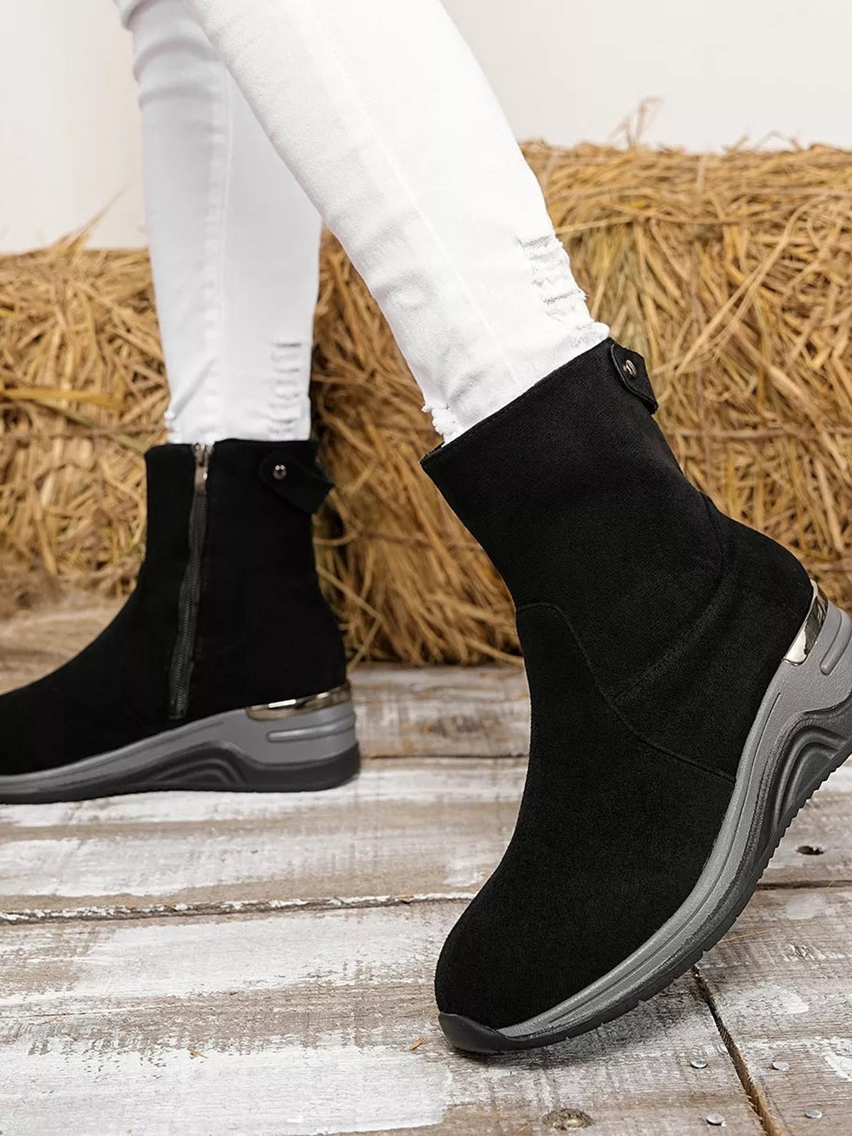 A model wears black suede ankle boots with sleek ankle-high silhouettes, side zippers, sculpted wedge heels, and durable rubber soles.