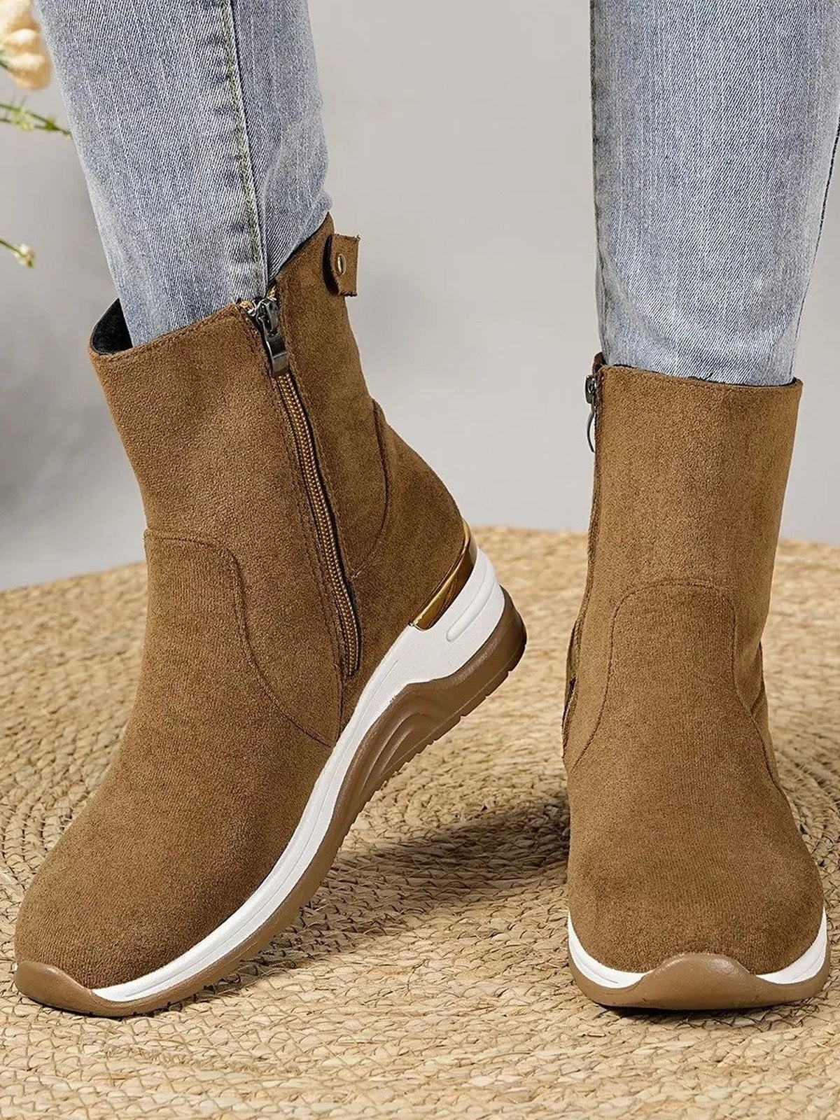 Model wears brown suede ankle boots with side zippers, rounded toes, and contrasting white-and-brown rubber wedge heels over light blue jeans.