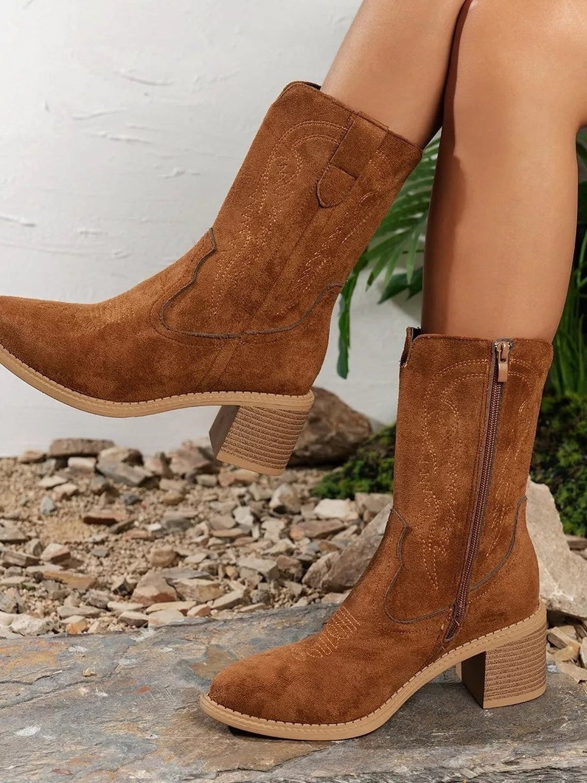 Model wears brown suede-style western boots with tall shafts, stitched detailing, side zippers, pointed toes, and sturdy mid-height block heels.