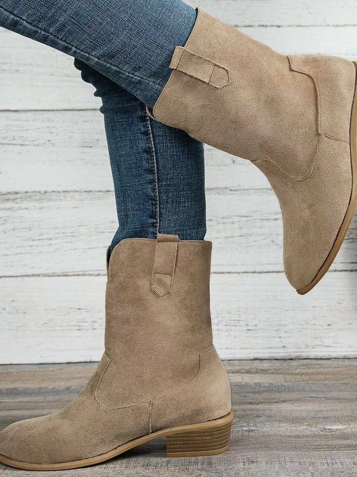 A model in blue jeans wears tan suede-look western boots with rounded toes, decorative ankle straps, tall shafts, and stacked mid block heels.