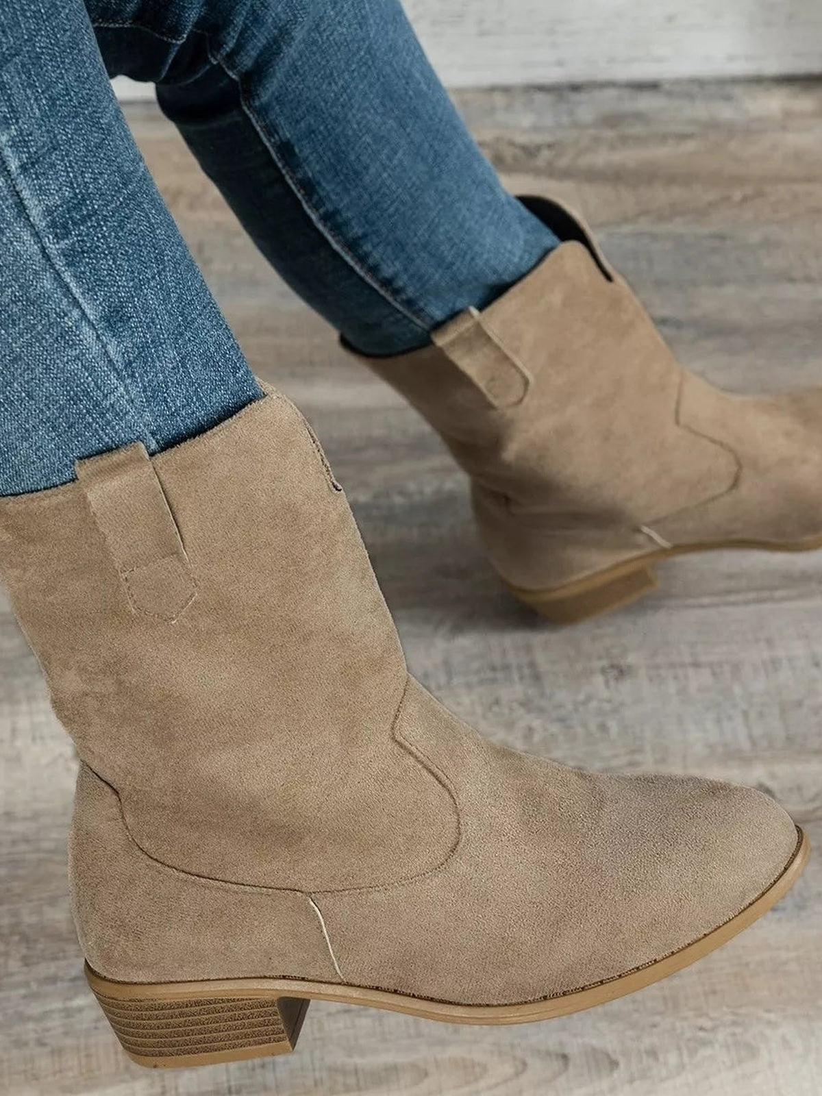 A model wears tan suede block heel Western boots with pointed toes, mid-height stacked heels, curved panel stitching, and pull-on shaft styling.