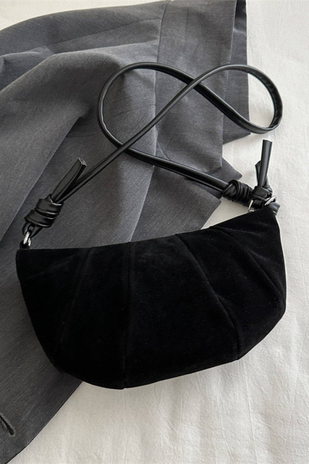 Black suede croissant-shaped shoulder bag with a softly curved, gathered paneled silhouette and long adjustable strap.