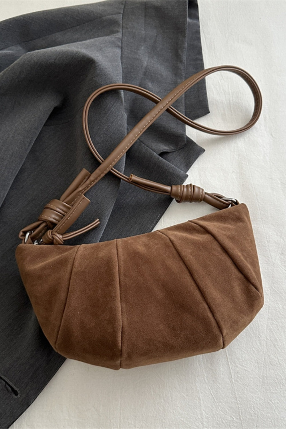 Brown suede croissant-shape shoulder bag with a softly curved, gathered paneled silhouette and long adjustable strap.