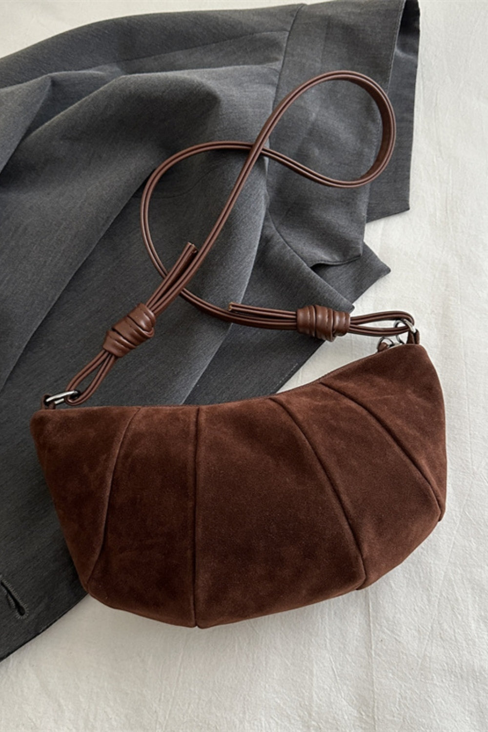 Brown suede croissant-shaped shoulder bag with a softly curved, gathered paneled silhouette and long adjustable strap.
