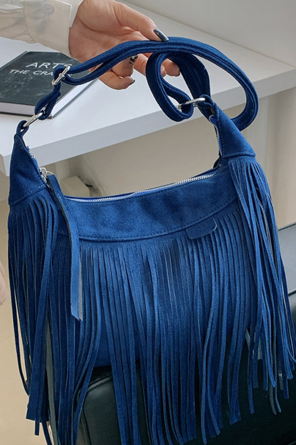 Deep blue suede shoulder bag with a softly curved silhouette, adjustable strap, zip closure, and long layered fringe along the sides and front.
