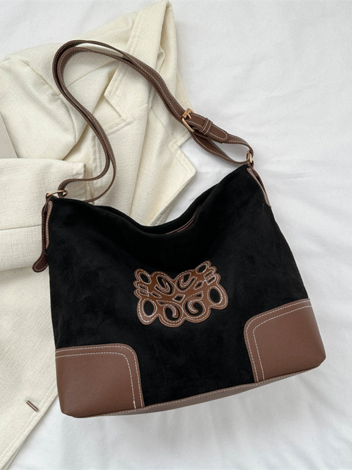 Black suede patch tote bag with a softly shaped silhouette, brown PU leather base panels, decorative stitched applique, and an adjustable shoulder strap.
