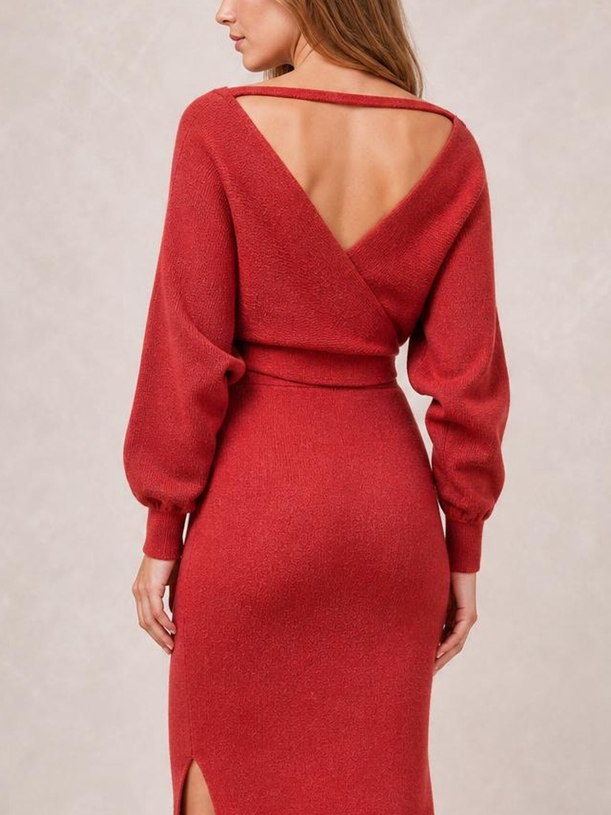 Model shown from the back in a red sweater dress with a surplice V-back, long sleeves, tied waist, fitted silhouette, and side slit.