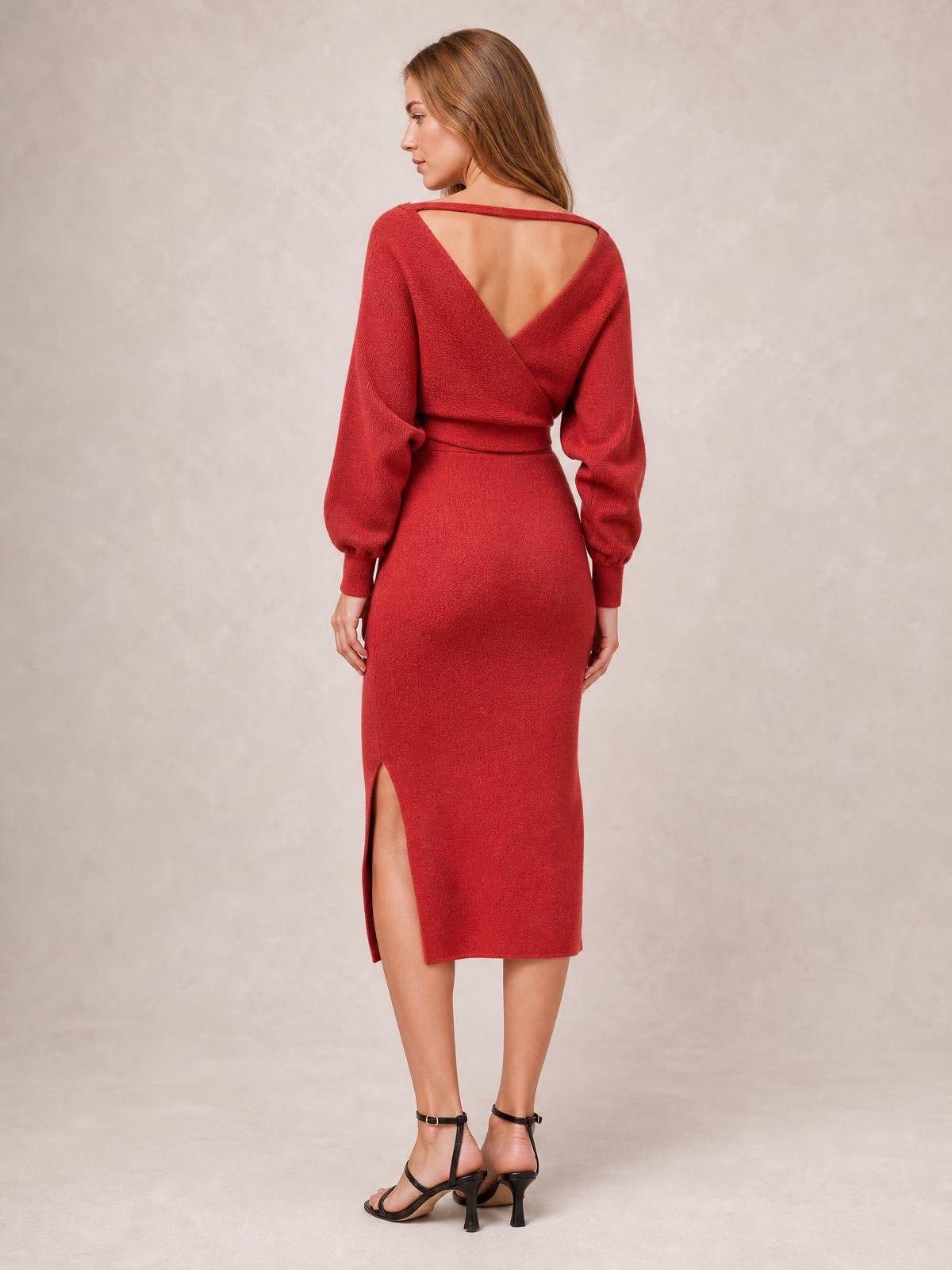 Model shown from the back in a red sweater dress with a surplice wrap bodice, tied waist, long sleeves, fitted midi silhouette, and side slit.