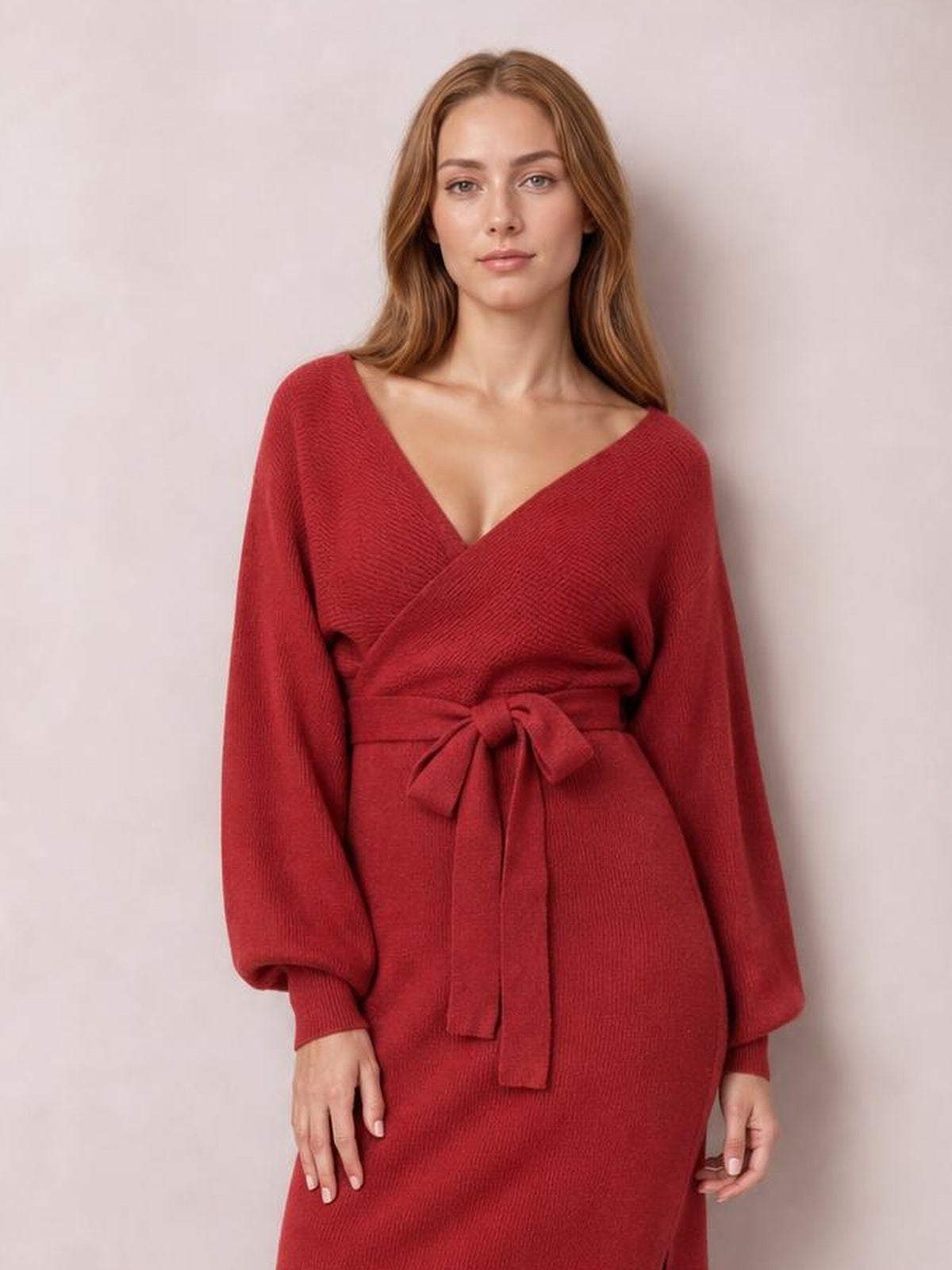Model stands facing forward in a burgundy sweater dress with a surplice V-neck, long sleeves, tied bow waist, and a gently fitted silhouette.