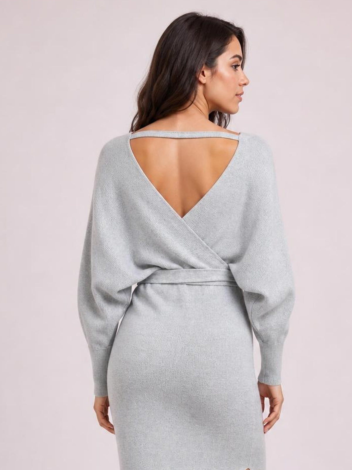 Model shown from behind wearing a light gray sweater dress with a deep V-back, long sleeves, wrap-style waist tie, and fitted midi silhouette.