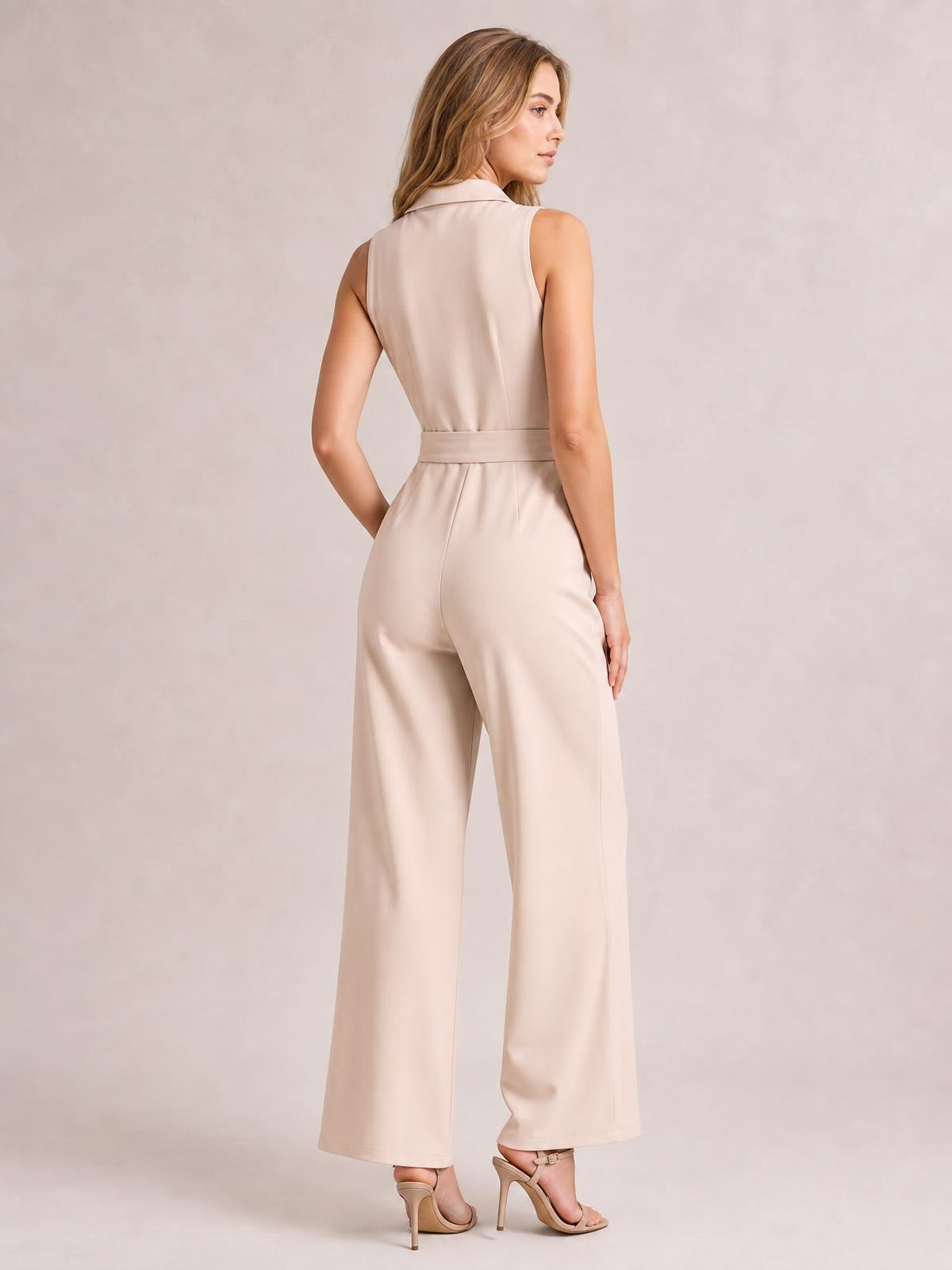 Model wearing a beige sleeveless jumpsuit with a belted waist, back seam detailing, and relaxed wide-leg trousers, posed in profile from behind.