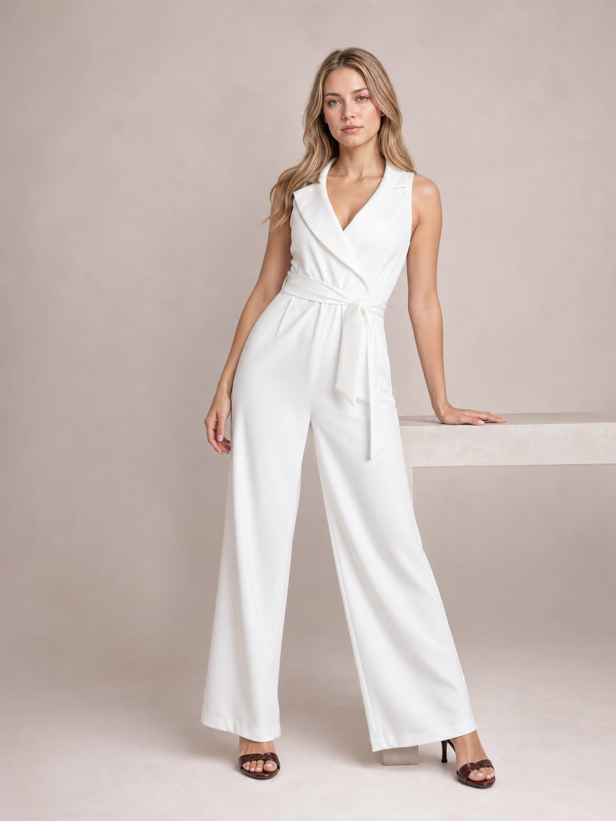 Model poses in a white sleeveless surplice jumpsuit with a tied waist, tailored wrap front, and flowing wide-leg silhouette.