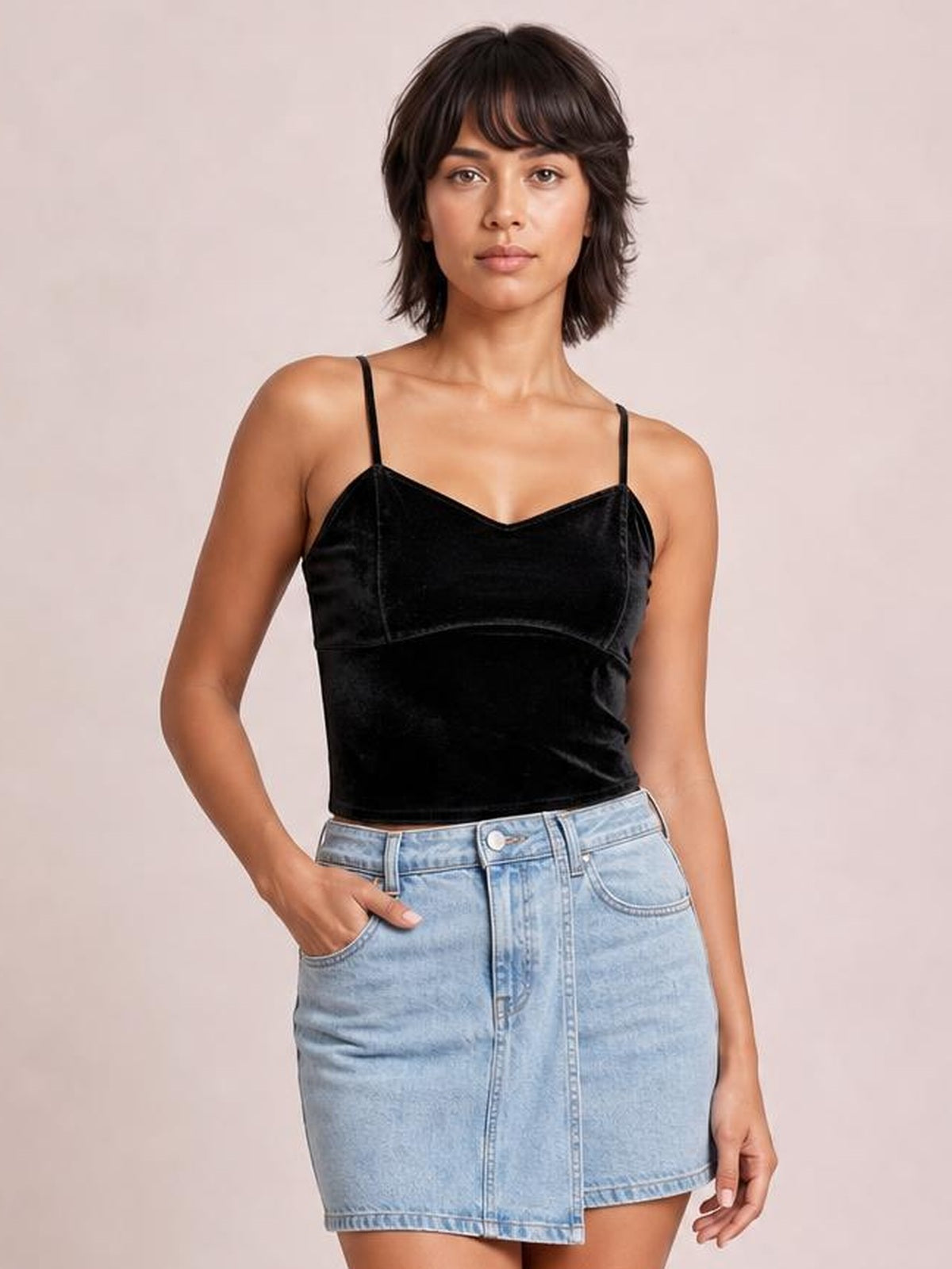 A model poses in a black sweetheart neck cropped cami with thin straps, a fitted silhouette, and seamed bust construction, paired with a denim skirt.