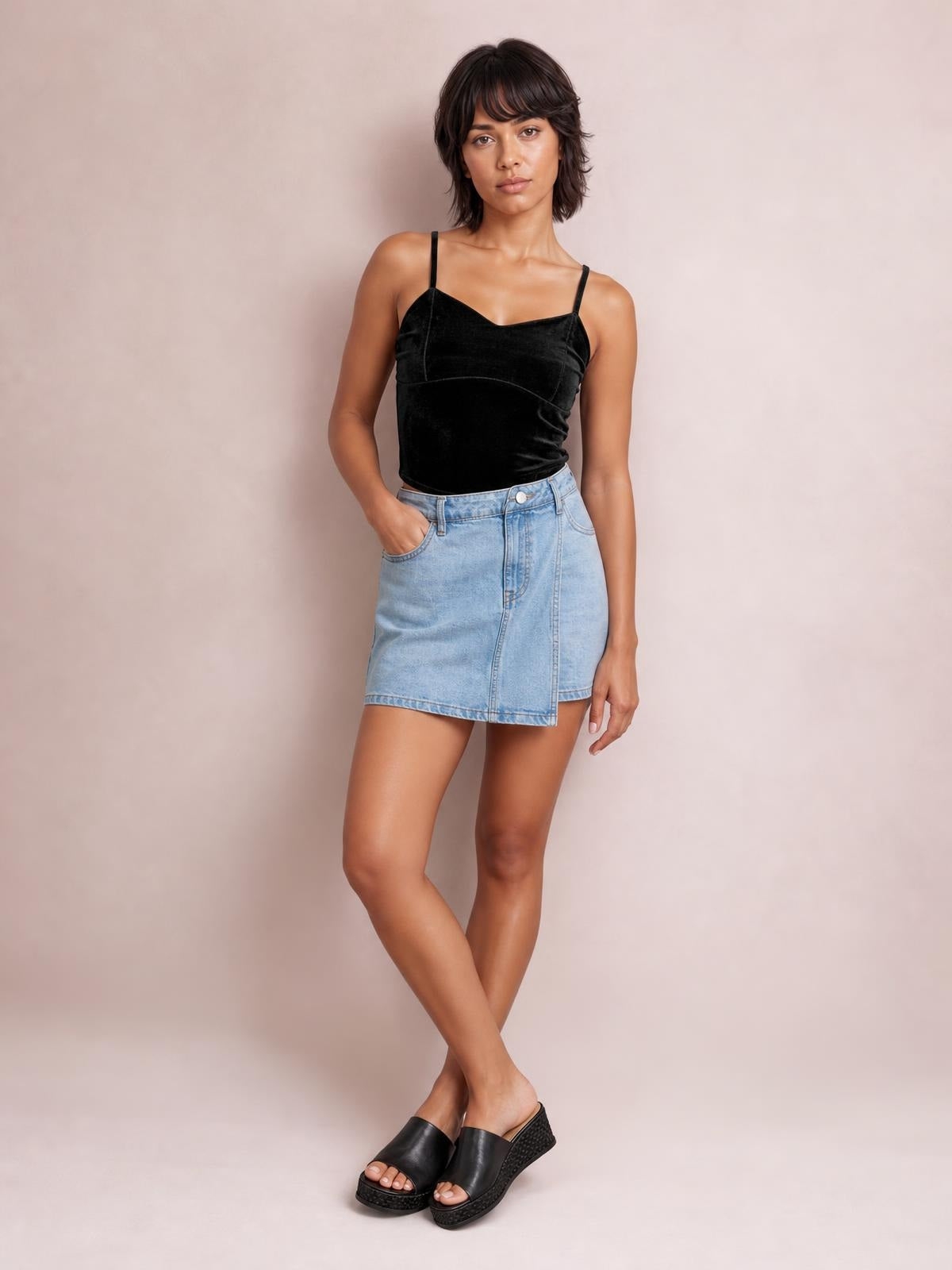 A model poses with crossed legs and one hand in her pocket, wearing a fitted black sweetheart-neck cropped cami with thin shoulder straps.