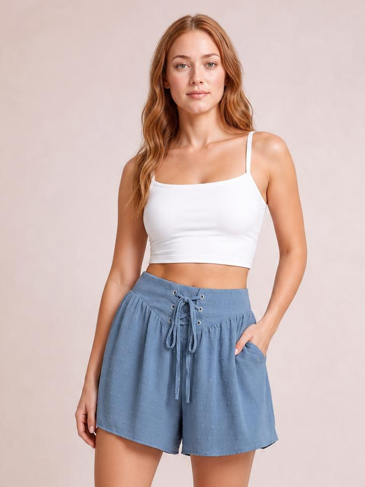 A woman modeling a white crop top and blue denim shorts against a solid pale pink background.