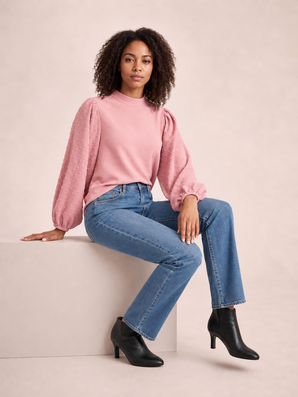 A model sits in a pink Swiss dot mock neck blouse with voluminous balloon sleeves, gathered cuffs, and a relaxed silhouette.