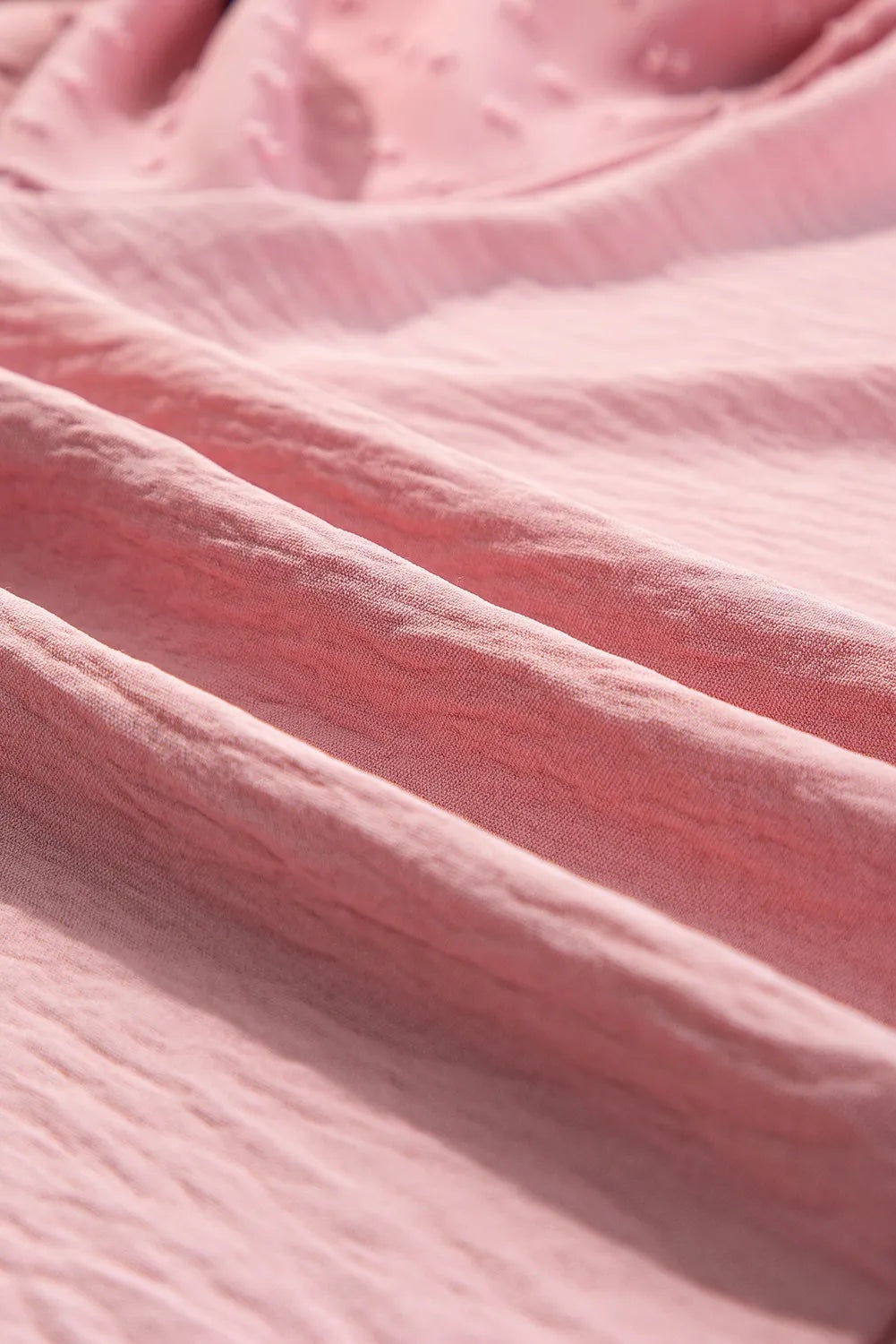 Close-up of soft pink blouse fabric showing gently gathered folds and a subtle textured finish.